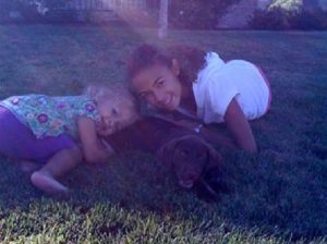 Two girls with their favorite chocolate Lab puppy